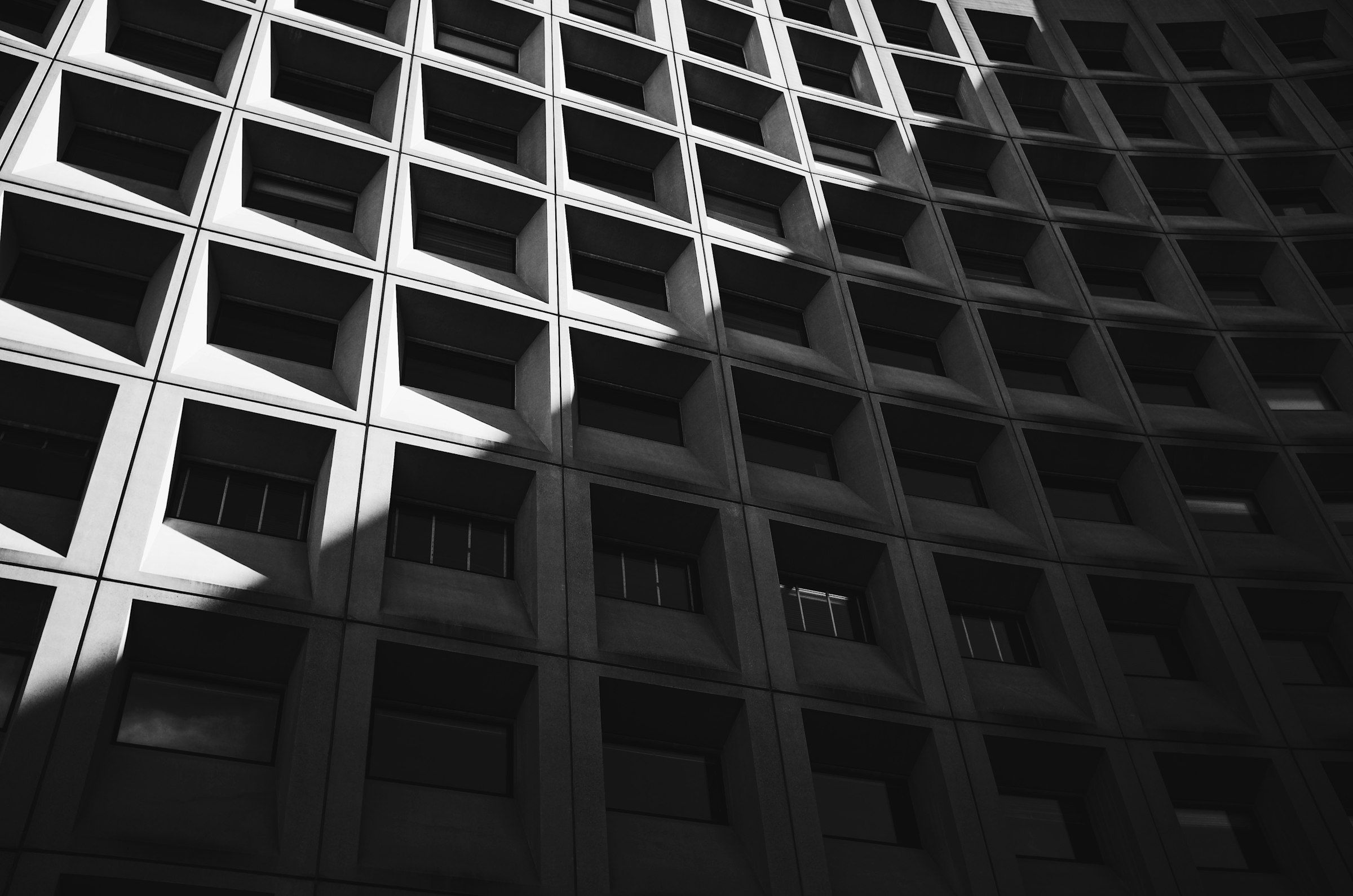 Brutalistische Betonfassade mit tiefen Fensterrastern im harten Licht, schwarzweiß